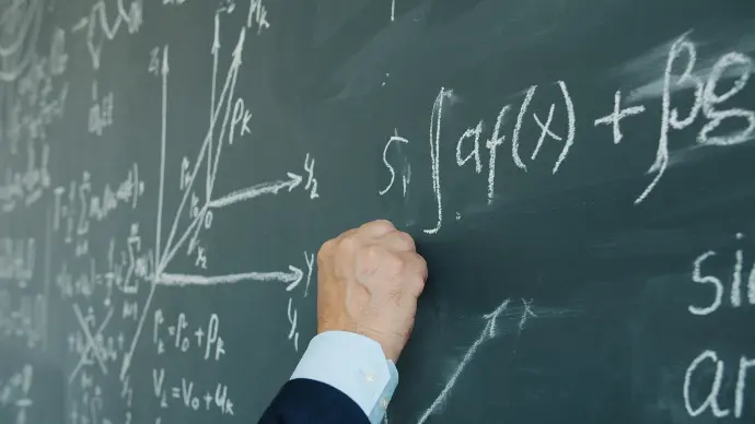 Hand writing mathematical formulas on a chalkboard.